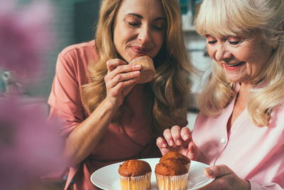 Cheerful daughter and mother preparing muffins at kitchen