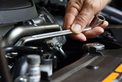 Cropped hand of mechanic repairing car engine with wrench