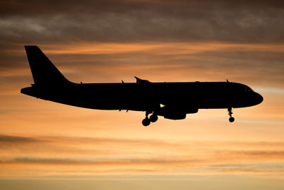 Silhouette airplane flying against sky during sunset