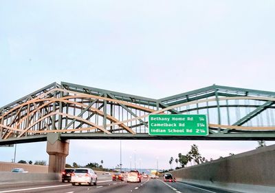 Road sign by bridge against sky