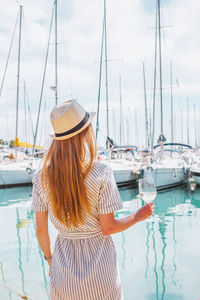 Long hair woman in hat, with wine glass in hand standing on sea, yachts background. nice, france