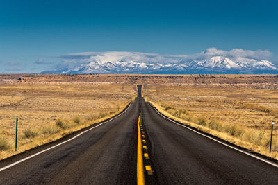 Empty road leading towards mountain against sky