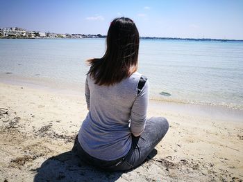 Rear view of woman sitting on shore at beach during sunny day