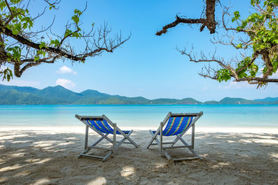 Deck chairs on beach against sky