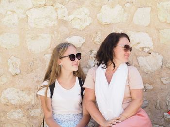 Mother and daughter wearing sunglasses while sitting against wall