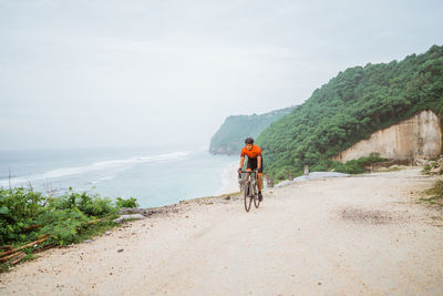 Rear view of man riding bicycle on road against sky