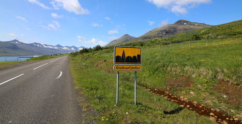 Sign board on grassy field by road against sky