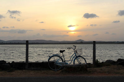 Bicycle by sea against sky during sunset