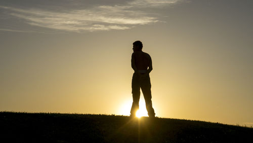Rear view of silhouette man standing on field at sunset