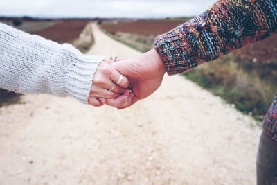 Cropped image of friends holding hands on dirt road