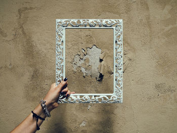 Close-up of hand holding ornate frame against weathered wall