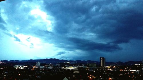 Illuminated cityscape against cloudy sky