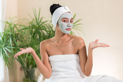 Portrait of young woman with facial mask gesturing in spa