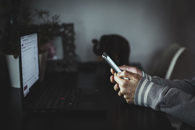 A woman works remotely from her home with a laptop and her phone.