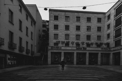 Rear view of man walking on street amidst buildings in city