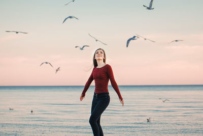 Woman looking at birds flying over sea against sky