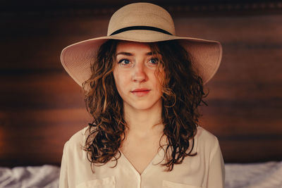 Portrait of young woman wearing hat standing against wall