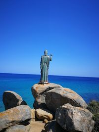 Statue on rock by sea against clear blue sky