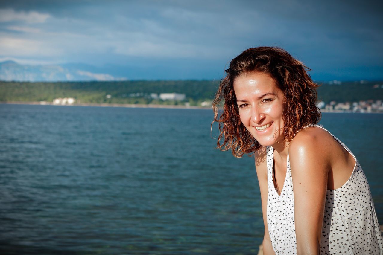 water, sea, smiling, one person, happiness, outdoors, looking at camera, day, young adult, nature, portrait, sky, young women, real people, people