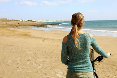 Rear view of woman with bicycle at beach against sky