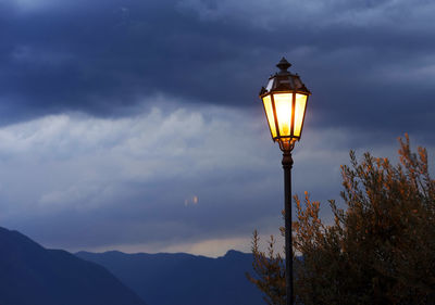 Low angle view of illuminated electric lamp against storm clouds