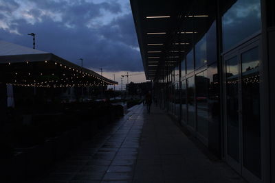 Illuminated street amidst buildings against sky at dusk