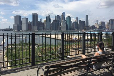 Woman sitting on bench against cityscape