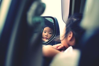 Portrait of girl reflecting in side-view mirror of car