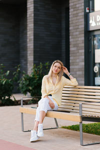 Stylish woman of thirty years old is sitting on a bench in the summer and resting in the city