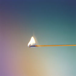 Close-up of burning matchstick against blue background