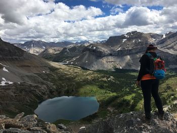 Rear view of hiker standing on lake against mountains