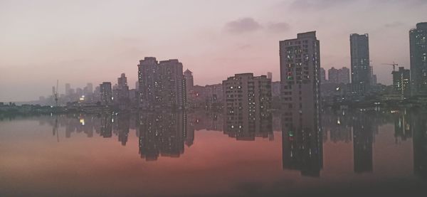 Reflection of buildings in river against sky at dusk