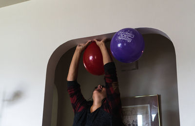 Rear view of woman holding balloons against wall at home