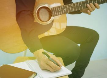 Midsection of man writing in book while playing guitar on seat
