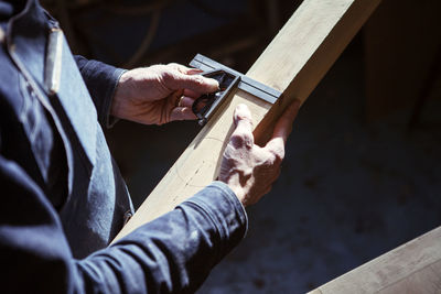 Midsection of carpenter measuring wooden plank in workshop