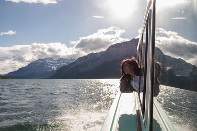 A woman tourist on a boat looking out with reflection and mountain in the background