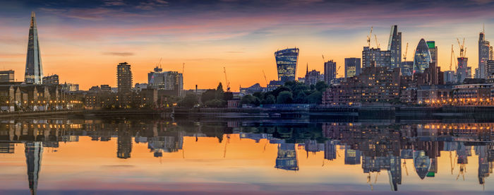 Reflection of modern buildings in lake during sunset