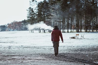 Rear view of man walking on snow field