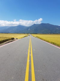 Empty road leading towards mountains against sky