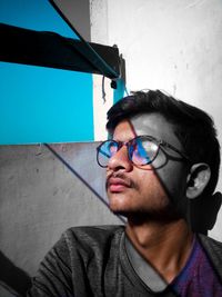 Portrait of young man wearing eyeglasses against wall