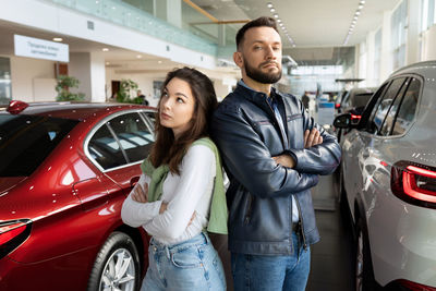 Angry couple standing with arms crossed in car showroom