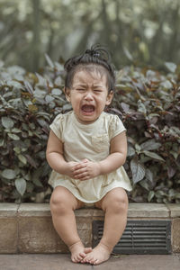 Cute baby girl crying while sitting against plants