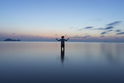 Man standing in sea against sky during sunset