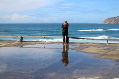 Rear view of woman standing at beach against sky