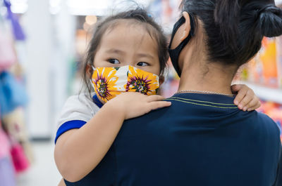 Mother carrying daughter wearing mask at supermarket