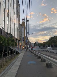 Road amidst buildings in city against sky during sunset