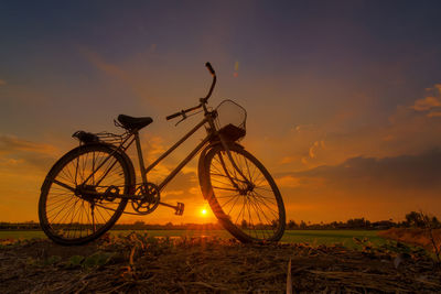 Low angle view of cycle on land against sky during sunset