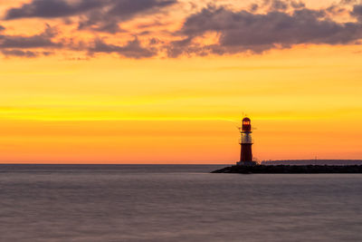 Lighthouse by sea against orange sky