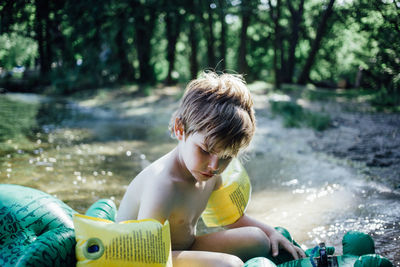 Shirtless boy wearing water wings on pool raft at lakeshore