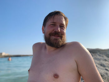 Portrait of shirtless man at beach against sky